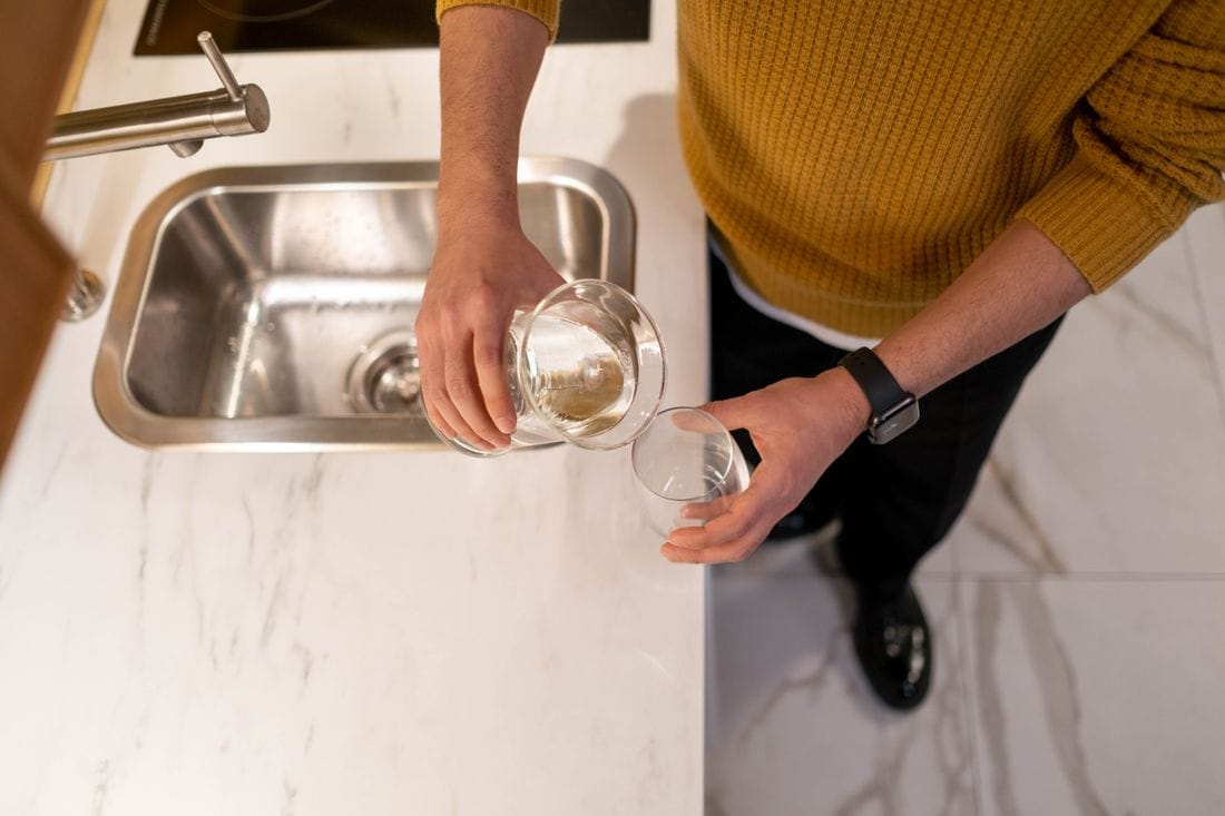 Pessoa serve água de jarra em copo de vidro na cozinha